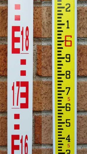 Two sides of a modern surveyor's levelling rod.Metric graduations on the left, imperial on the right.